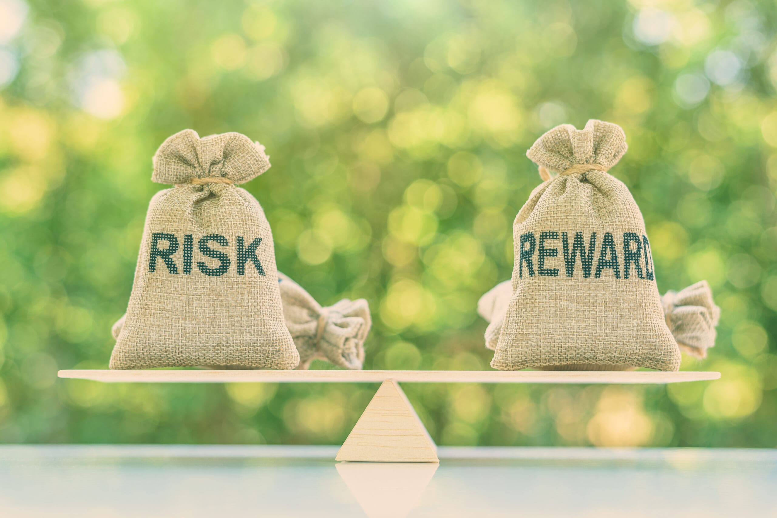 Risk reward ratio / risk management concept : Risk and reward bags on a basic balance scale in equal position, depicts investors use a risk reward ratio to compare the expected return of an investment