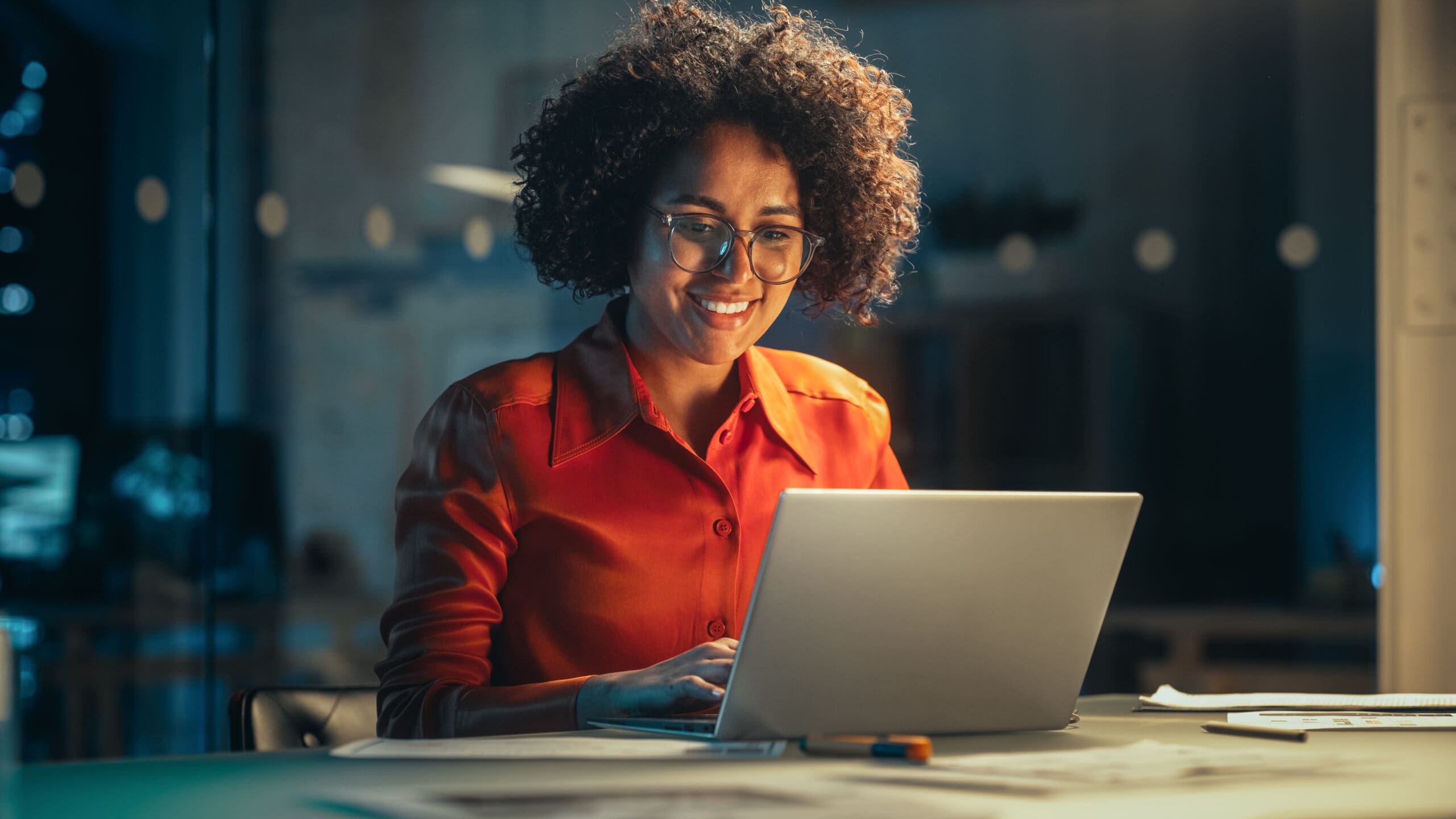 Young Black Female Working on Laptop Computer in Creative Office in the Evening. Multiethnic Project Manager Writing Emails, Getting Happy and Surprised When Receiving a Message from a Colleague.