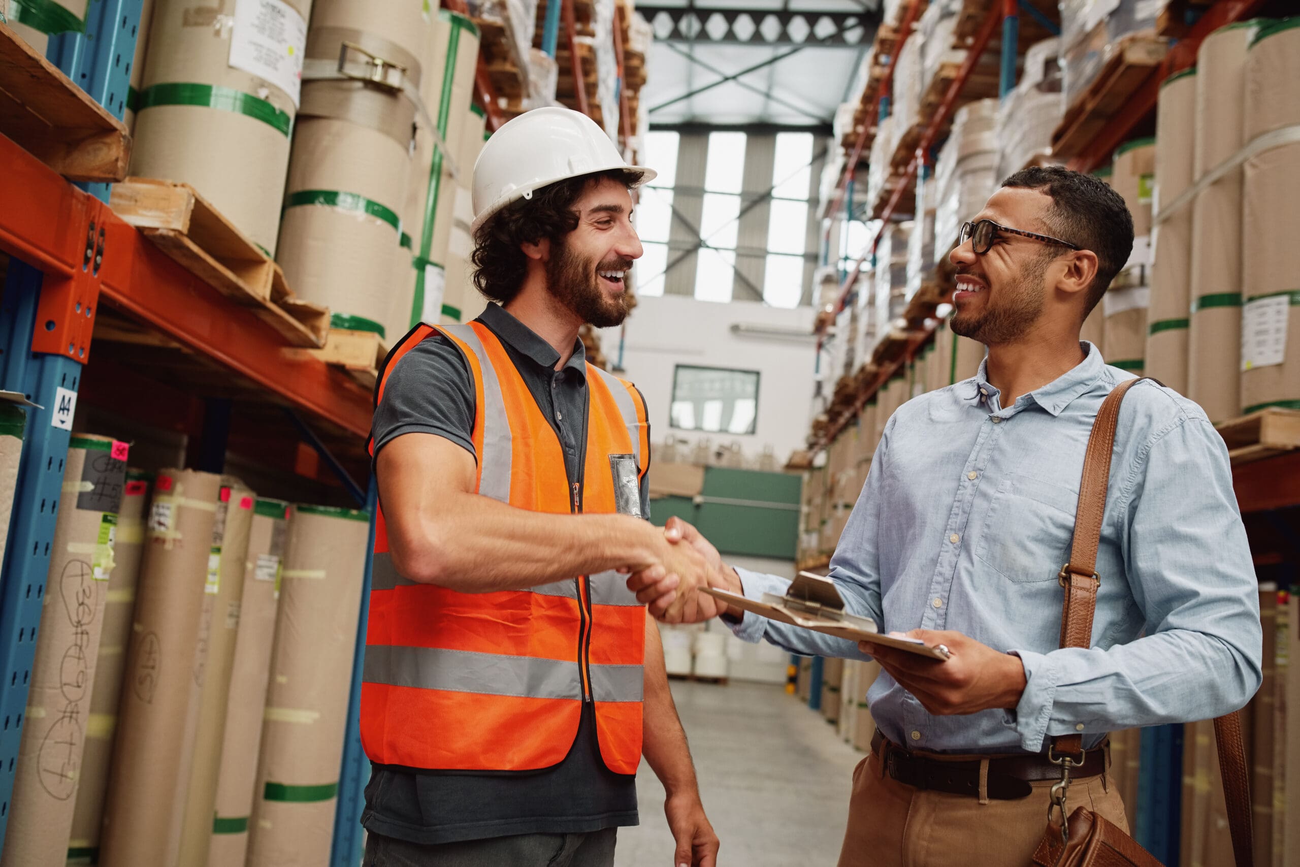 Happy handsome customer in formal clothing shaking hand of storage manager with clipboard after discussing contract