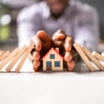 Man protects house from falling dominoes with his hands