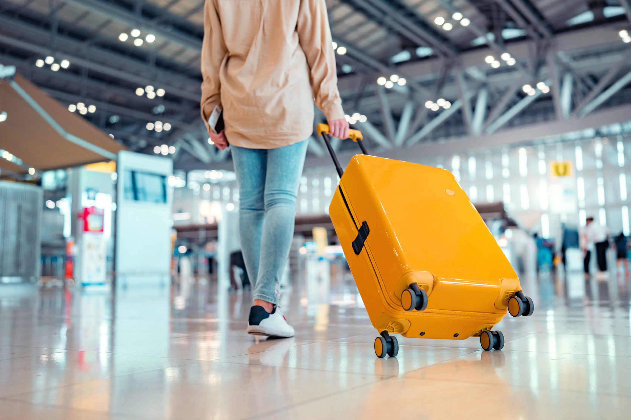 Young female traveler passenger walking with a yellow suitcase at the modern Airport Terminal, Back view of woman on her way to flight boarding gate, Ready for travel or vacation journey