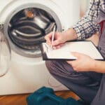 Repairman is repairing a washing machine on the white background. Entering malfunction