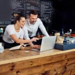 Two cafe owners working together planning supply orders on laptop