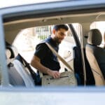 Handsome male passenger smiling and getting on a rideshare car while talking to the female driver