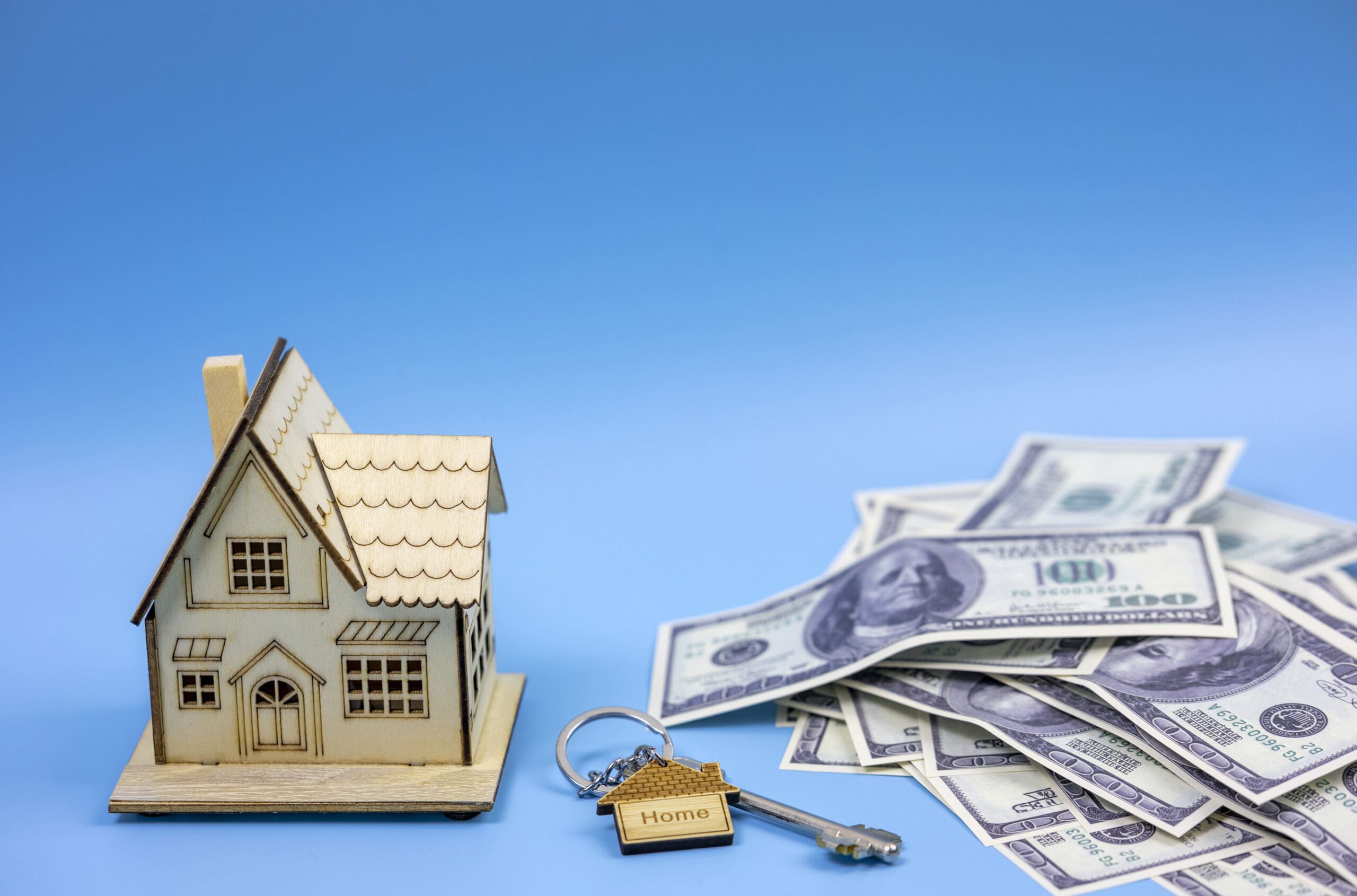 key with a key chain from a wooden house and a miniature house a pile of American money, real estate or real estate investment