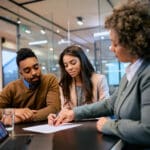 African American woman and her husband signing mortgage agreement during a meeting with their bank manager.