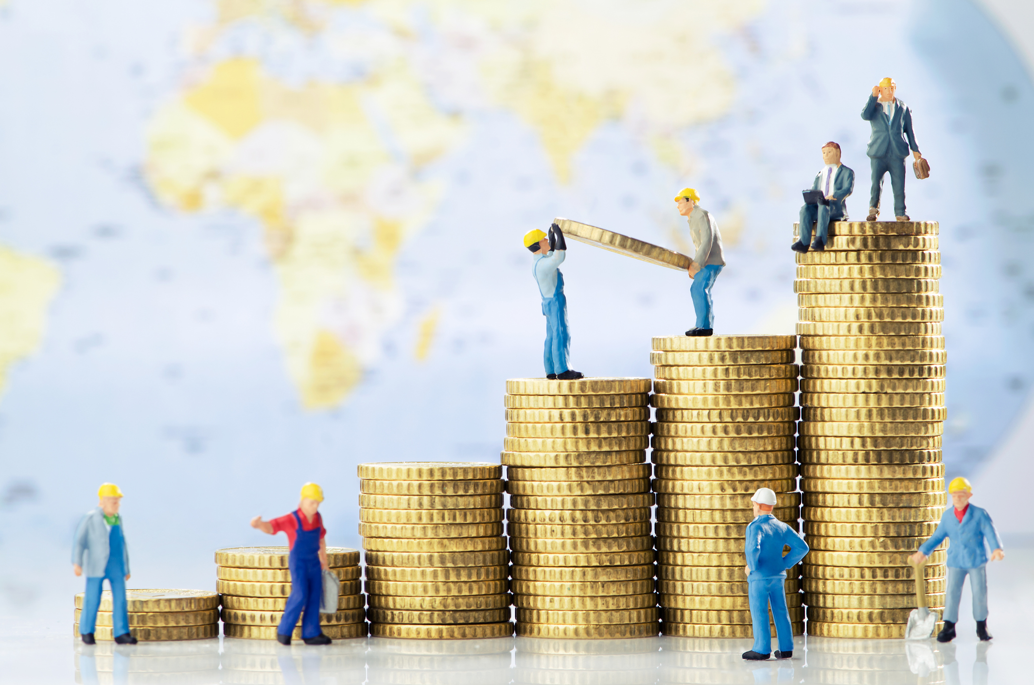 Little business men figurines on top of a growing pile of gold coins