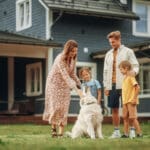 Portrait of a Cheerful Family Couple with Kids, Playing and Petting a Beautiful White Golden Retriever Dog. Happy Successful People Standing on a Lawn in Their Front Yard in Front of the House.