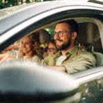 Portrait of a father driving a new car or having a test drive in the city while riding with his family. Parents and daughters spending vacation traveling by automobile and enjoying road trip.