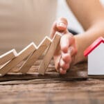 Close-up Of A Human Hand Stopping The Wooden Blocks From Falling On House Model