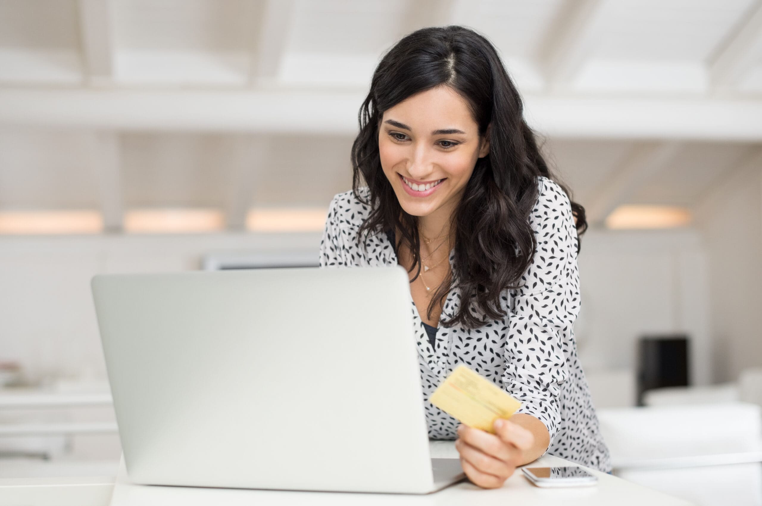 Happy young woman holding a credit card and shopping online at home. Beautiful girl using laptop to shop online with creditcard. Smiling woman using laptop and credit card for online payment.