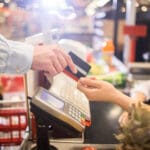 Side view close up of unrecognizable customer handing credit card to cashier paying via bank terminal at grocery store