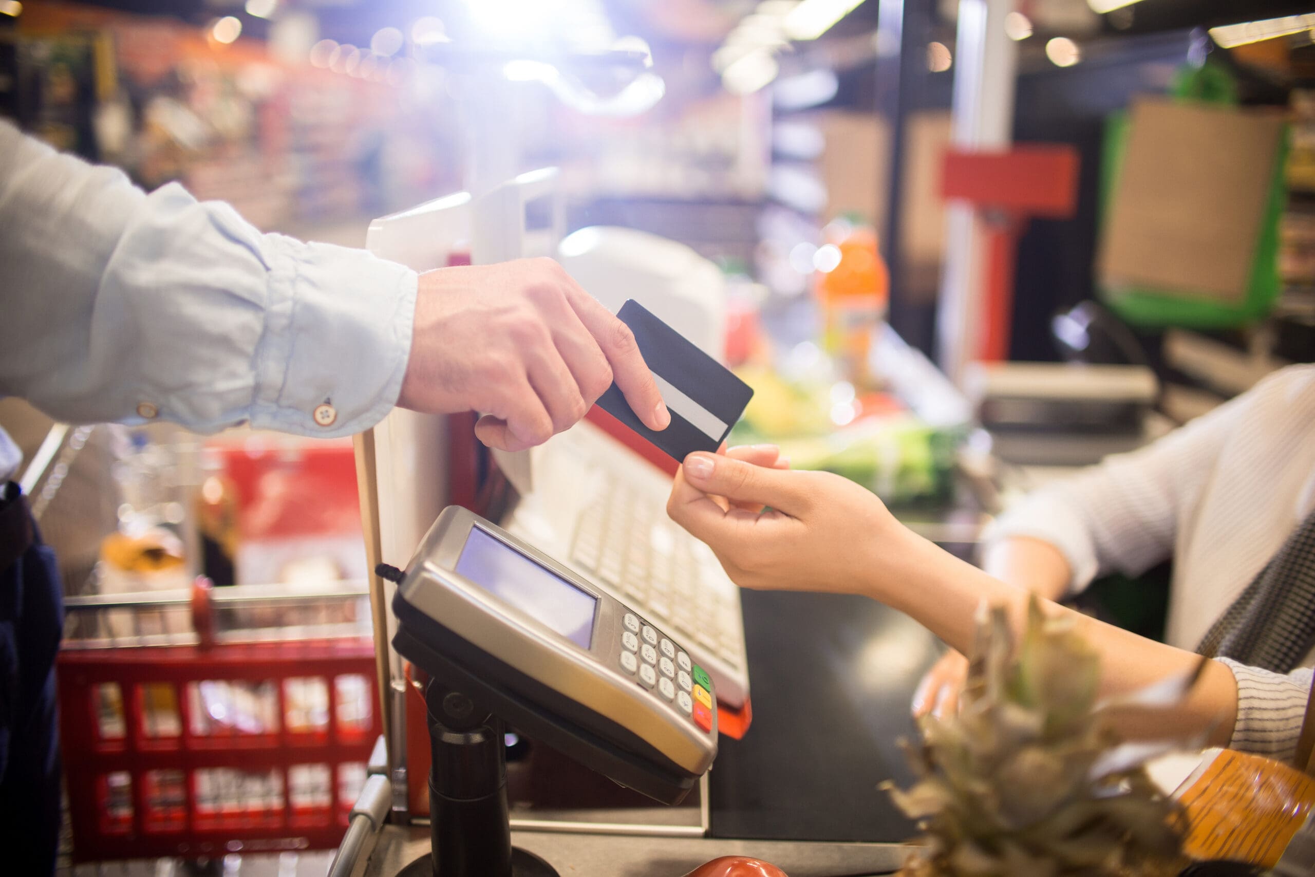 Side view close up of unrecognizable customer handing credit card to cashier paying via bank terminal at grocery store