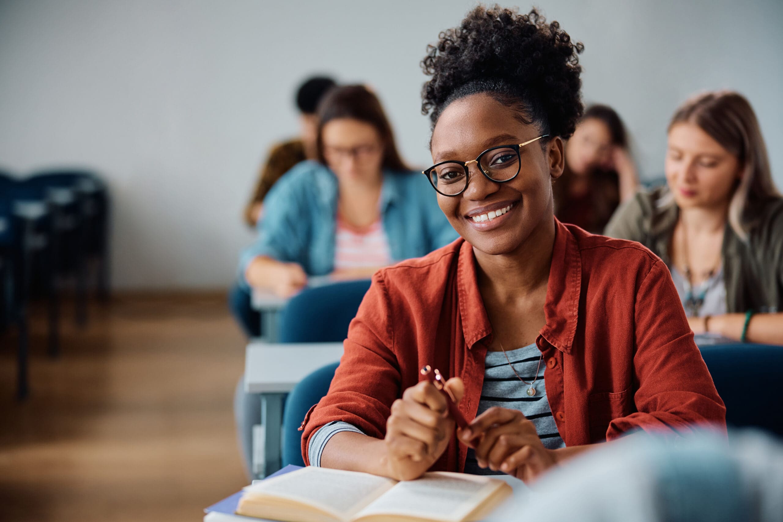 Happy African American woman attending a lecture in university classroom and looking at camera.