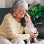 Senior woman exchange cuddles with her cavalier king Charles dog sitting together on home sofa. Pet therapy and best friend concept