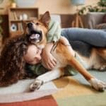 Portrait of young woman playing with happy dog fooling around on floor at home, copy space