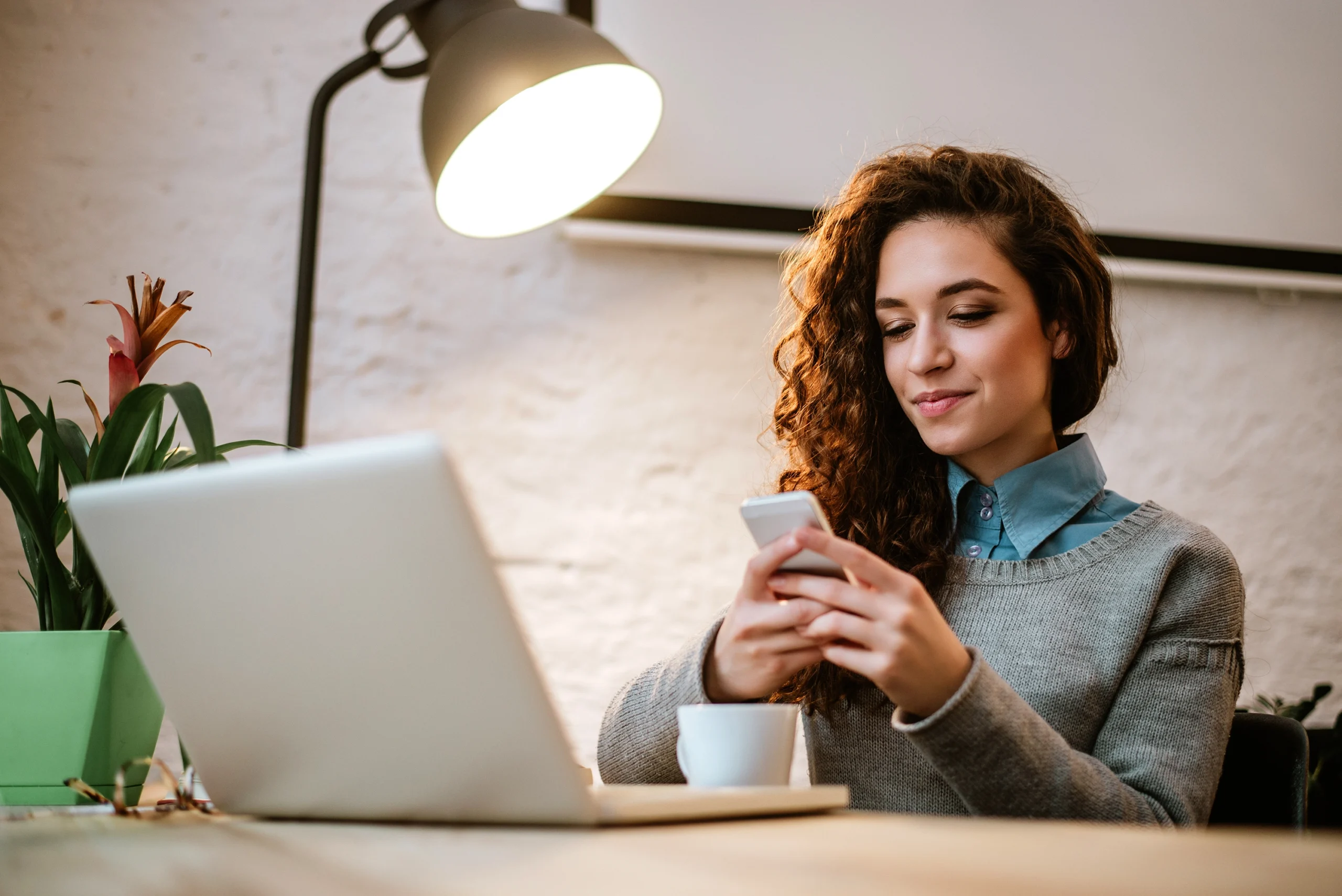 Young Woman Reading About How To Build An Emergency Fund At Her Desk With Laptop And Coffee