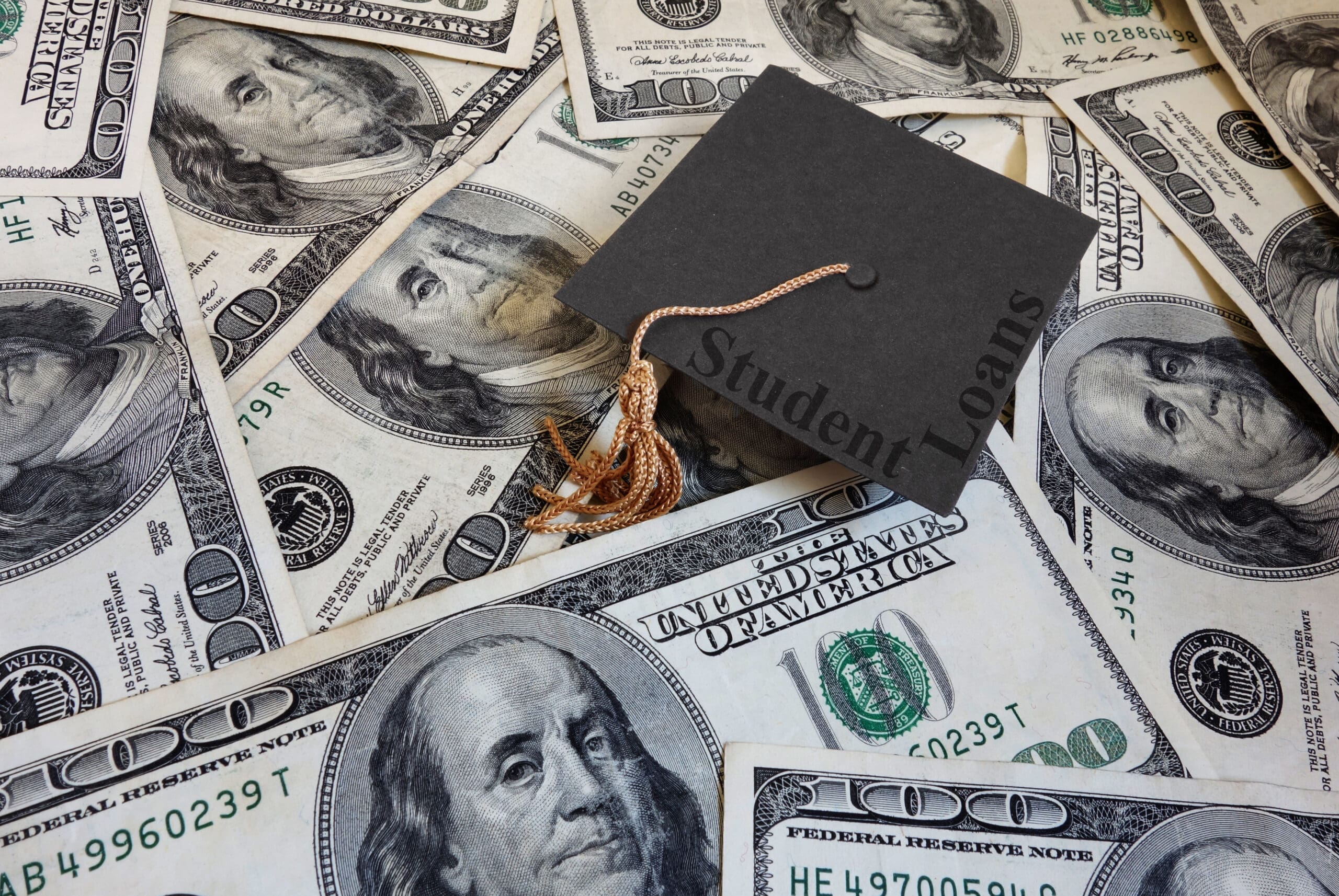 Miniature graduation cap with Student Loans text, on assorted cash