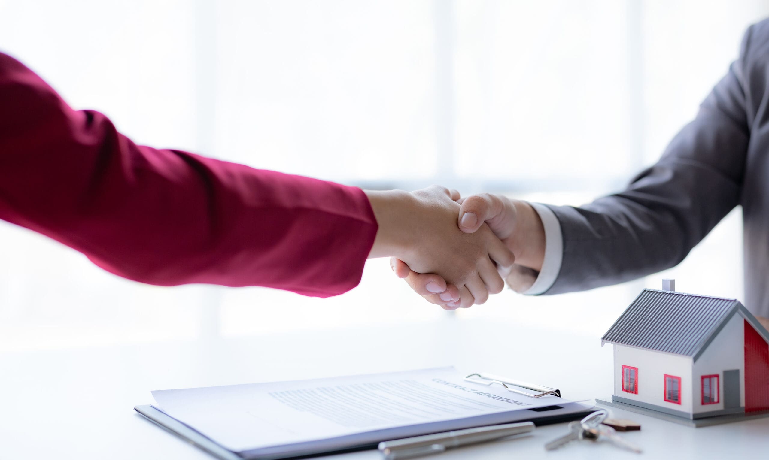 Real estate agent shakes hands with a client to sign a home purchase contract congratulating the client on the purchase.