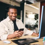 Young Black Man At Desk Looking For 7% Interest Savings Accounts