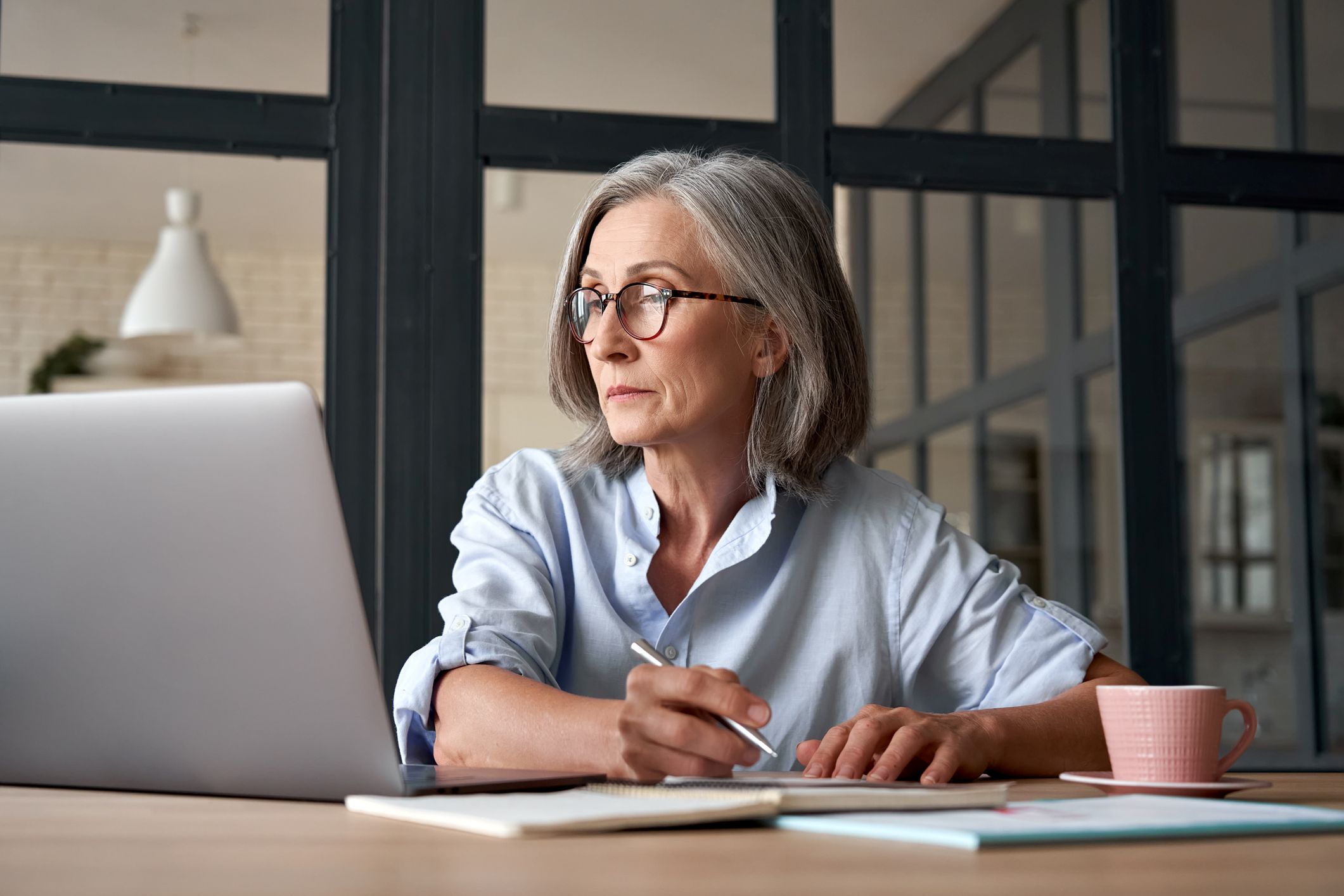 A serious mature older adult woman looks at her laptop while working from home.