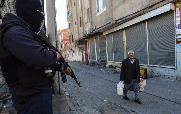 An elderly man walks past an armed government soldier during clashes in central Diyarbakir on March 17, 2016 | Ilyas Akengin/AFP via Getty Images