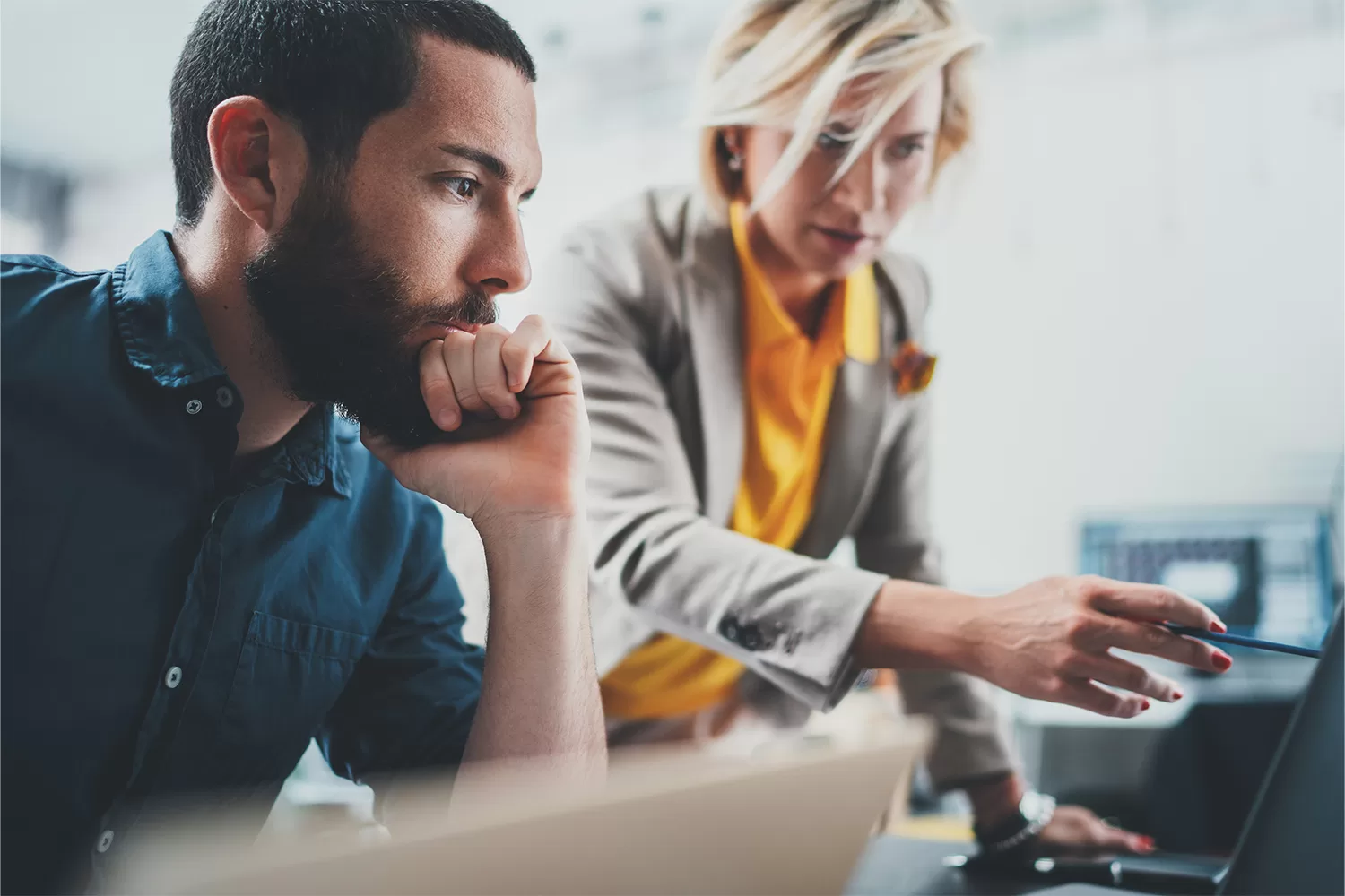 A photograph of two co-workers sitting at a desk and looking at a computer.