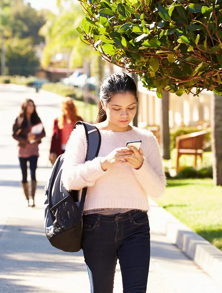 A photo of a student walking through campus whilst looking down at their phone.