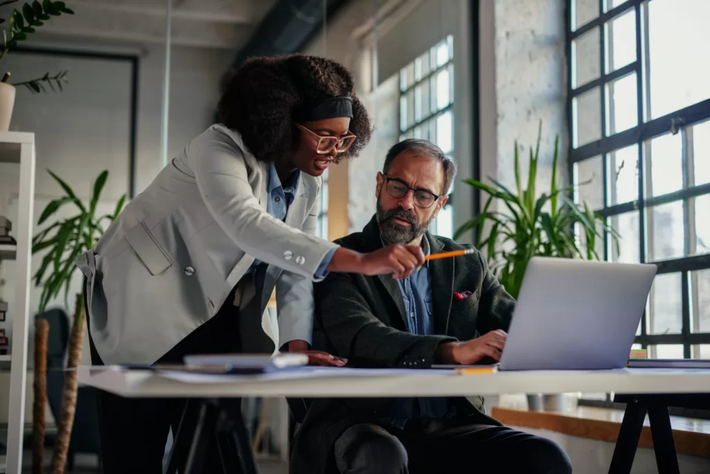 Two employees are having a discussion whilst gathered around a laptop.