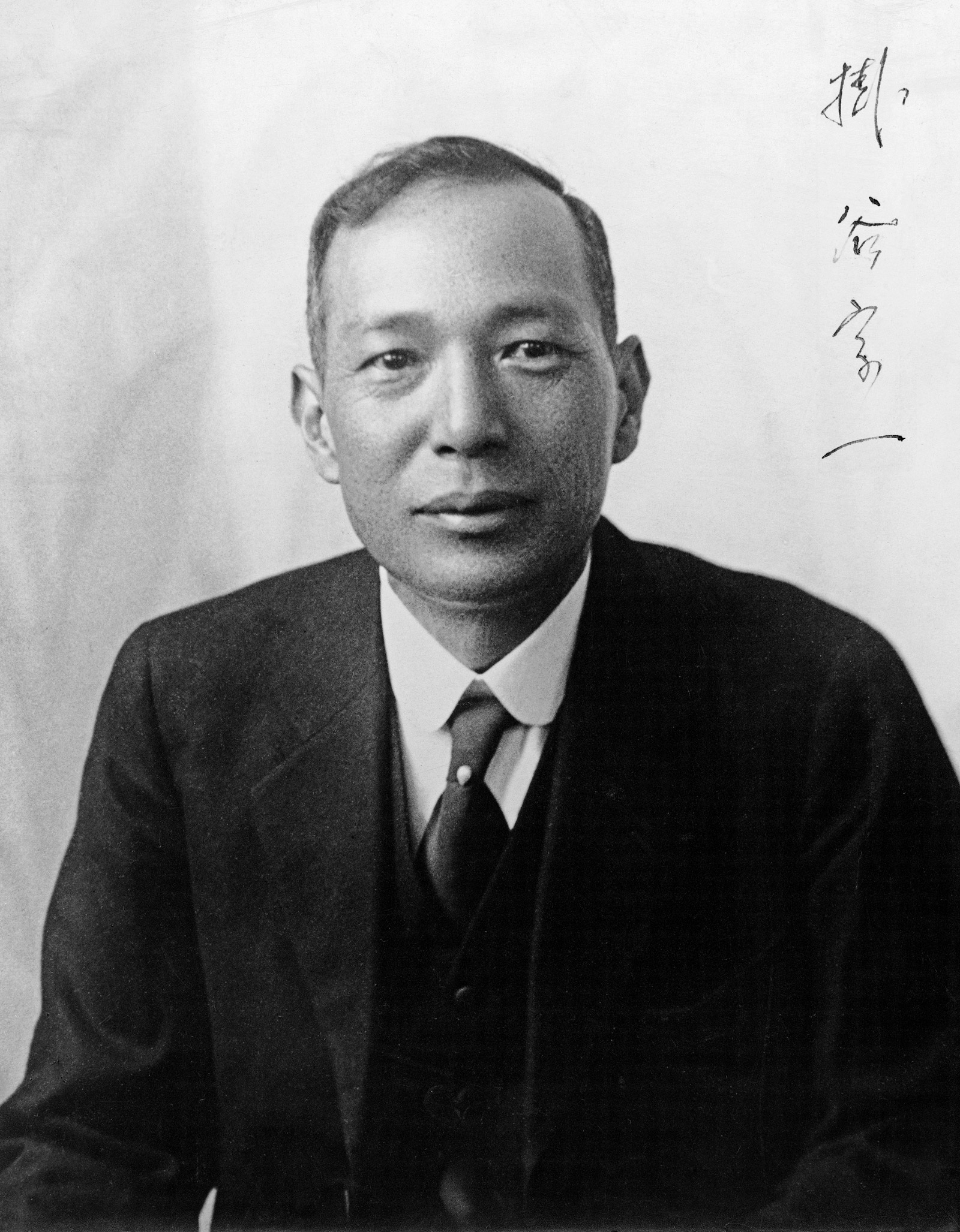 black and white photo of a fairly young Japanese man wearing a dark suit, vest, and tie. It is a formal portrait and there is writing in Japanese going down the right side of the photo.