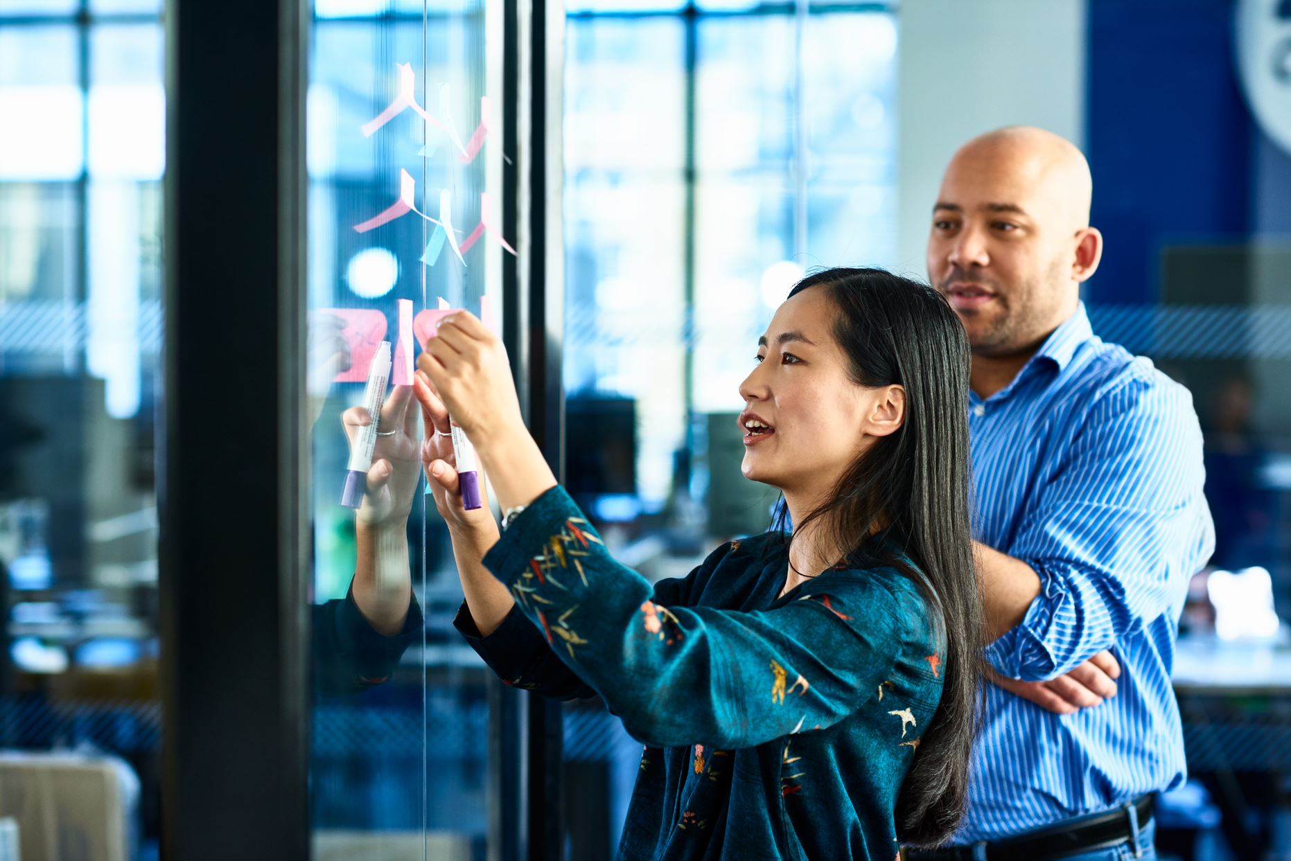 two people putting sticky notes on the glass