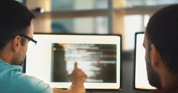 two people pointing at a computer with codes on the screen