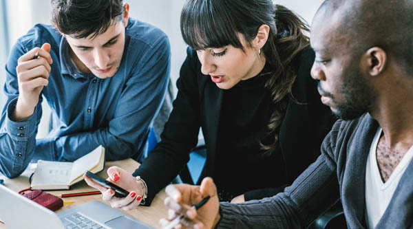 three people working together on one laptop in an office setting