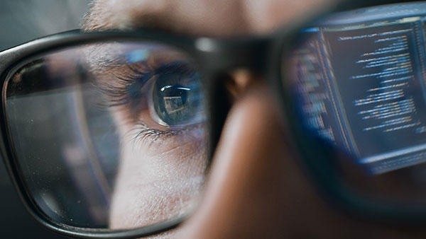 Man with glasses with the reflection of the monitor showing code