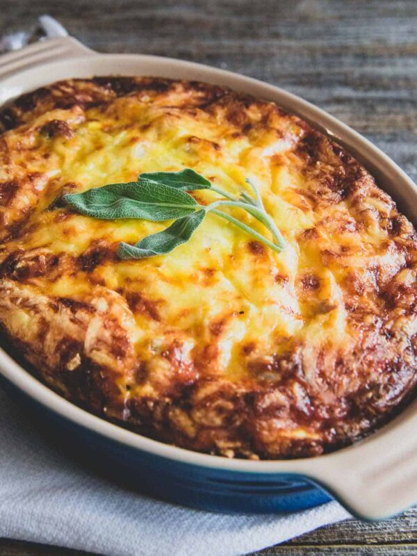 Cheesy potato breakfast casserole in a baking dish topped with sage leaves.