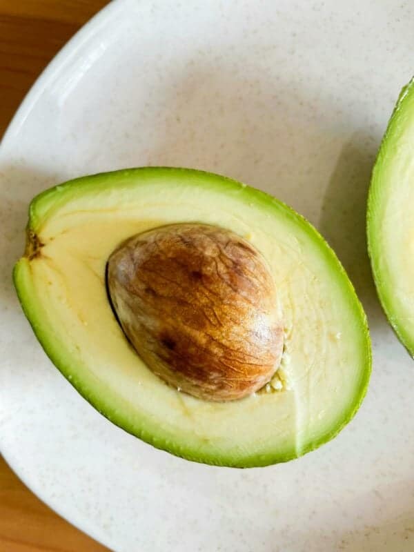 A halved Hass avocado with its pit intact on a white plate.