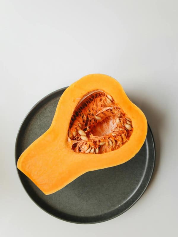 A halved butternut squash with visible seeds and vibrant orange flesh rests on a round, dark gray plate against a light background, inviting thoughts on how to freeze butternut squash for lasting freshness.