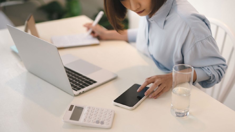 Asian woman on her phone in front of a laptop computer smb digital sales success