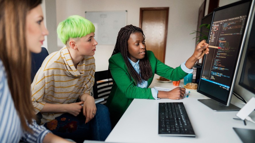 Photo of IT developers working to build AI apps. 3 people looking at a computer screen in an office setting.