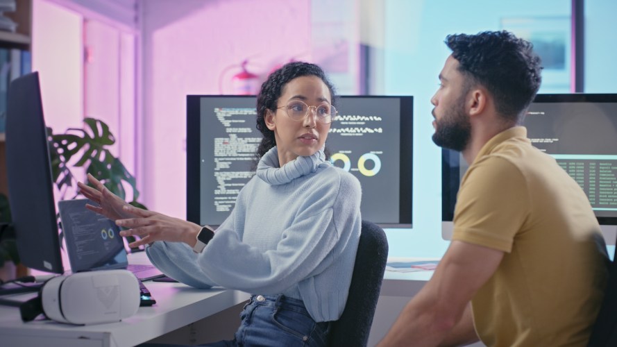 A female programmer talking with her male coworker at a desk in the office / software development lifecycle