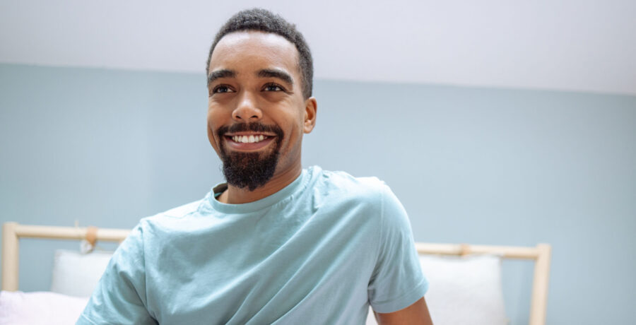 Handsome young African American man waking up in bed with smile