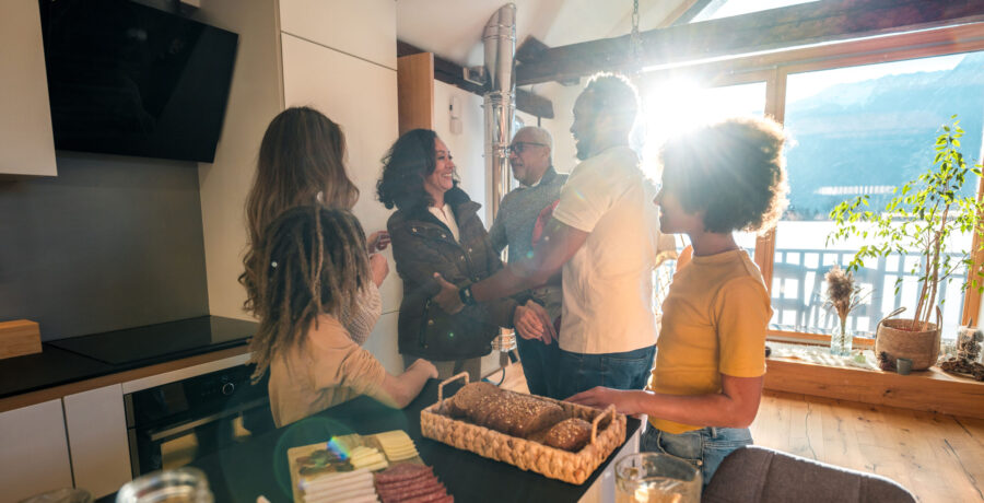 Mixed race grandparents enjoy a visit with their Caucasian and Black daughter, her husband and their mixed race children in a sunny, modern kitchen.