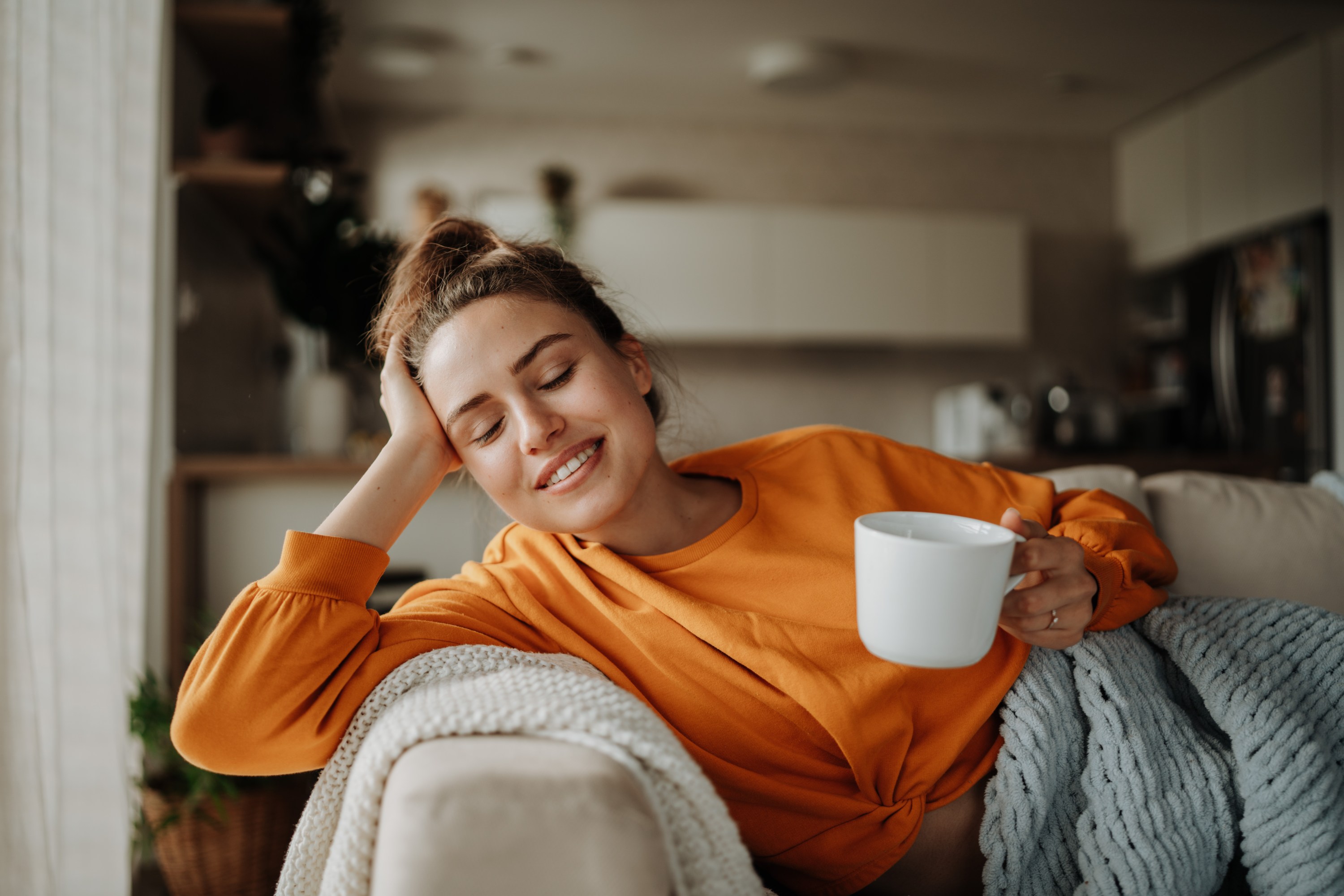 Young woman resting on sofa with blanket and cup of tea.