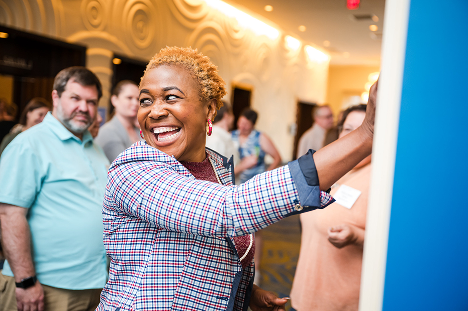 A teacher, smiling, is putting a post-it note on a chart at the Middle School Research Teachers Conference.