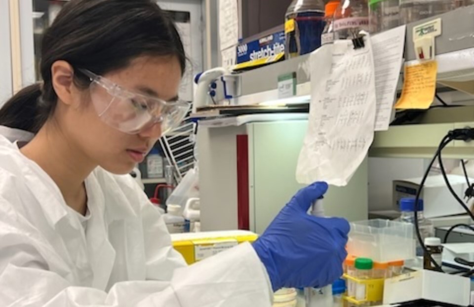 Claire Xu, wearing a white coat, performing work in the lab.