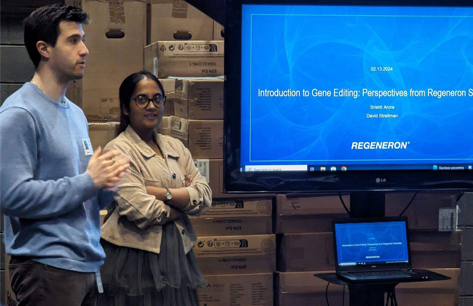 Two people are posed to the left of a presentation that explains research into gene editing.