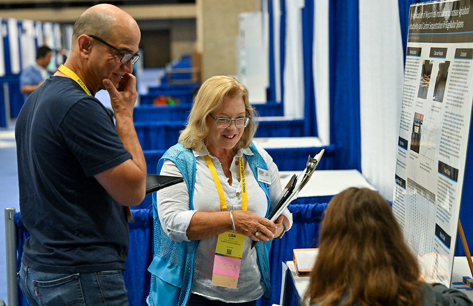 ISEF 2023 Dallas TX International Science and Engineering Fair - Display and Safety Volunteers talking with finalist about their project in the exhibit hall.