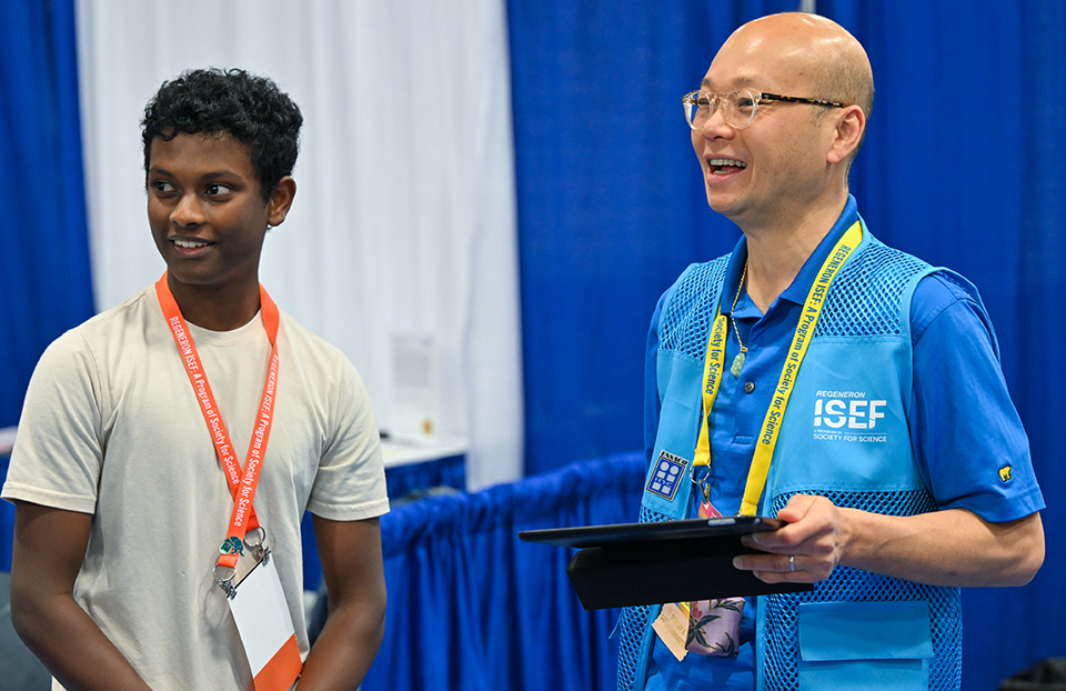 ISEF 2023 Dallas TX International Science and Engineering Fair - Display and Safety Volunteer talking with finalist about their project in the exhibit hall.