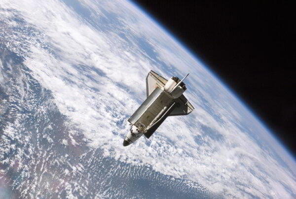 A photo of the Space Shuttle Atlantis seen in orbit around a cloudy blue Earth, below.