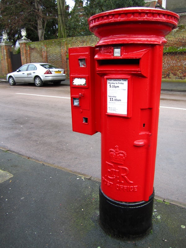 Red British postbox on a pavement with a car in background.